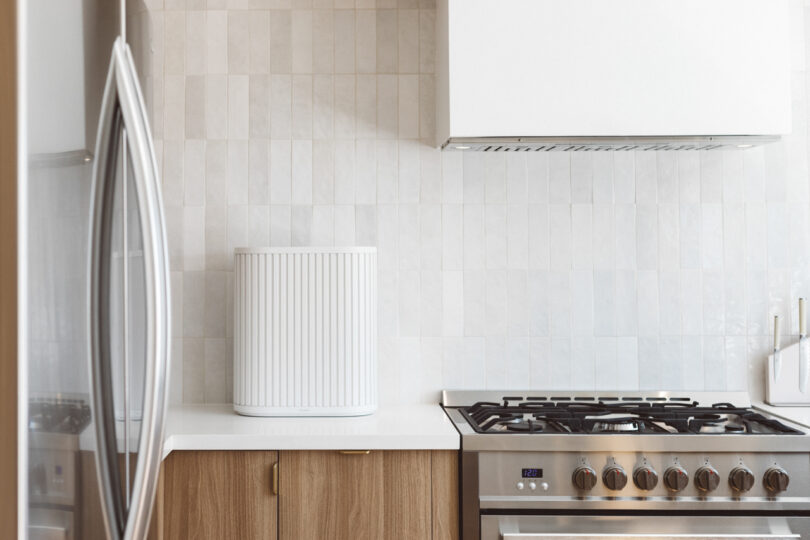 A modern kitchen with a stainless steel gas stove, white tile backsplash, white range hood, and a white appliance on a wooden countertop.