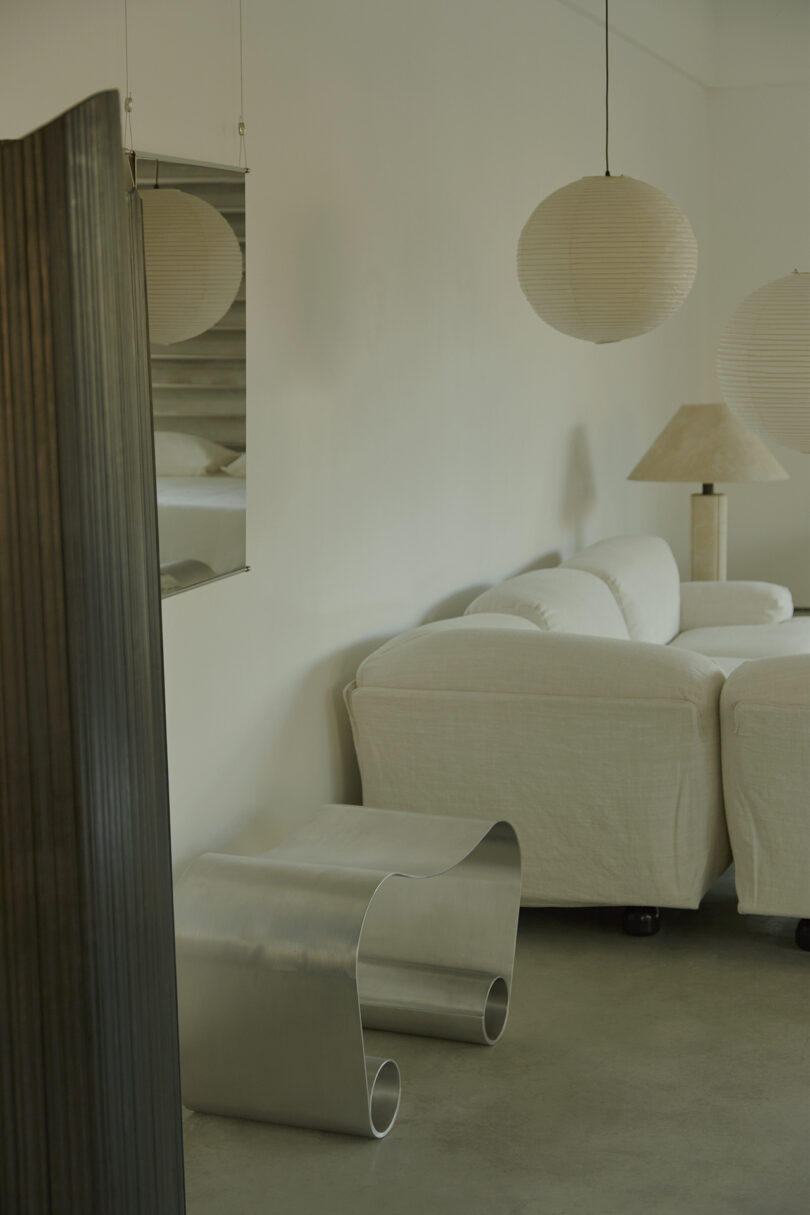 Minimalist living room with a white couch, paper pendant lights, a metallic side table, and a folded screen.