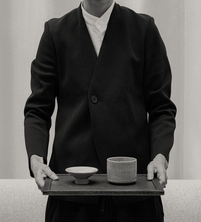 Person in a dark suit holding a wooden tray with two ceramic bowls.