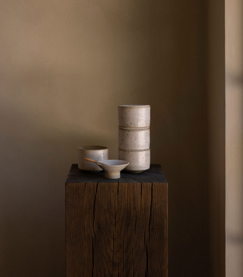 Ceramic bowls and plates stacked neatly on a rustic wooden pedestal against a neutral-toned background.