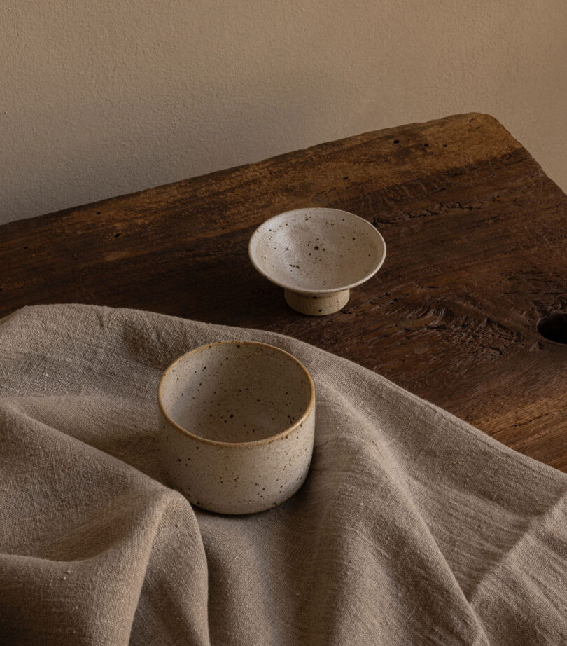 Two ceramic bowls on a wooden table, partially covered by a textured cloth.