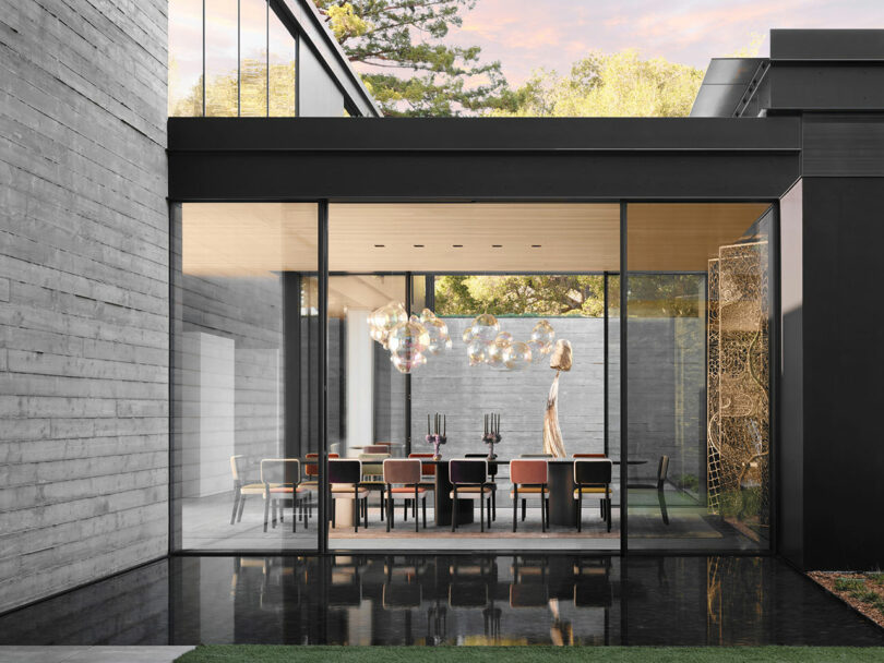 Modern dining room with a large glass wall, wooden ceiling, and a table set with chairs. Artistic lighting fixture hangs above the table.