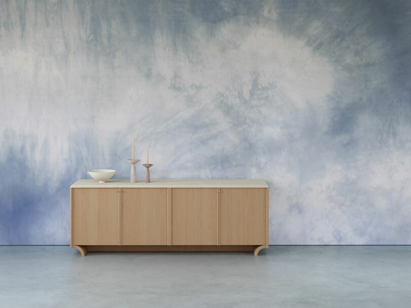 A wooden sideboard with decorative items stands in front of a blue and white abstract wall.