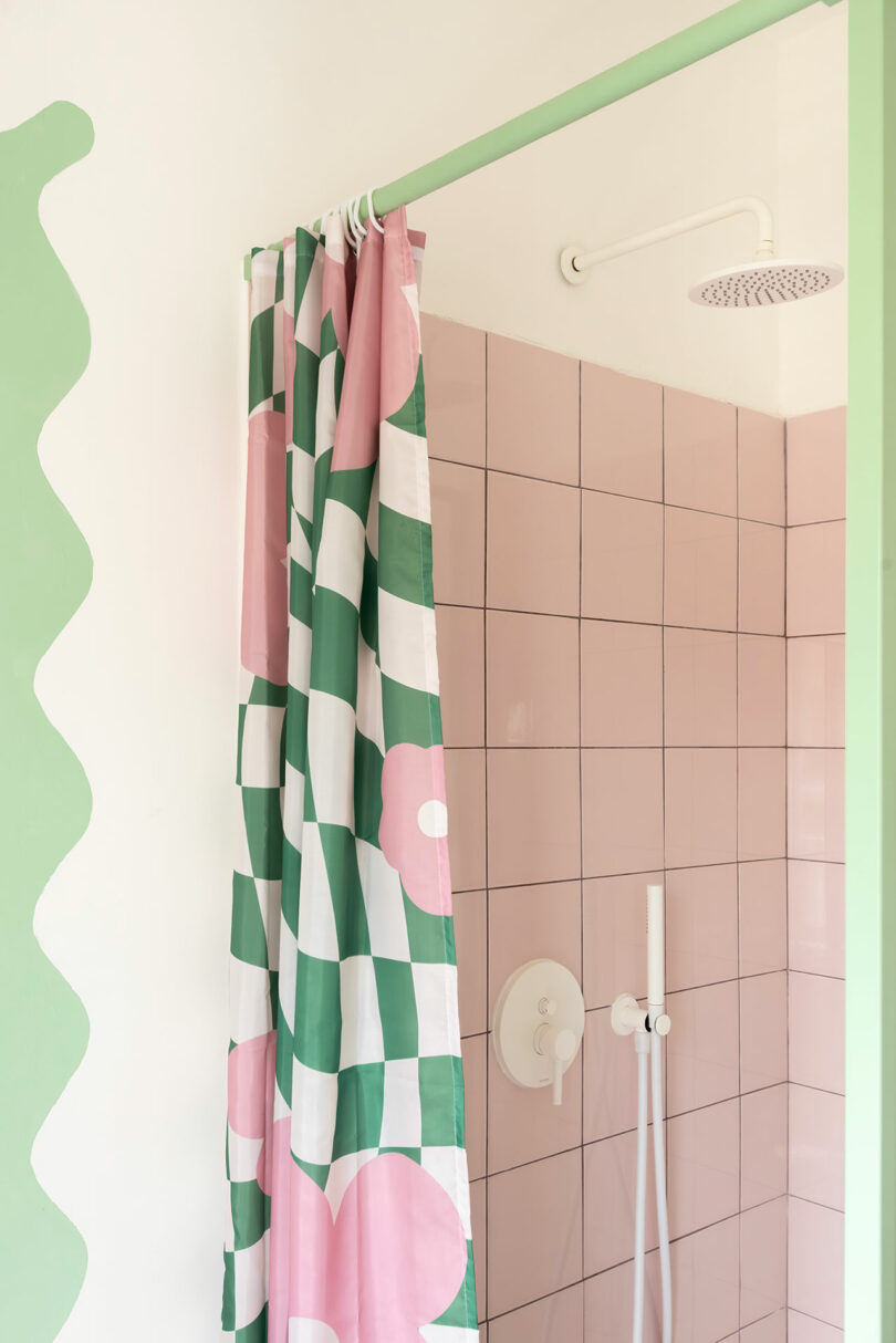 Shower with a pink tiled wall and a green and pink checkered shower curtain featuring floral patterns.