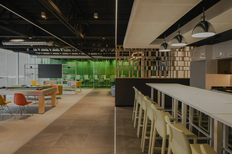 Modern office interior with a pool table, green chairs, and a long bar-style table with high chairs, surrounded by ambient lighting.