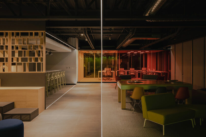 Modern office interior with a divided design featuring a lounge with green chairs on one side and a work area with red glass partitions on the other.