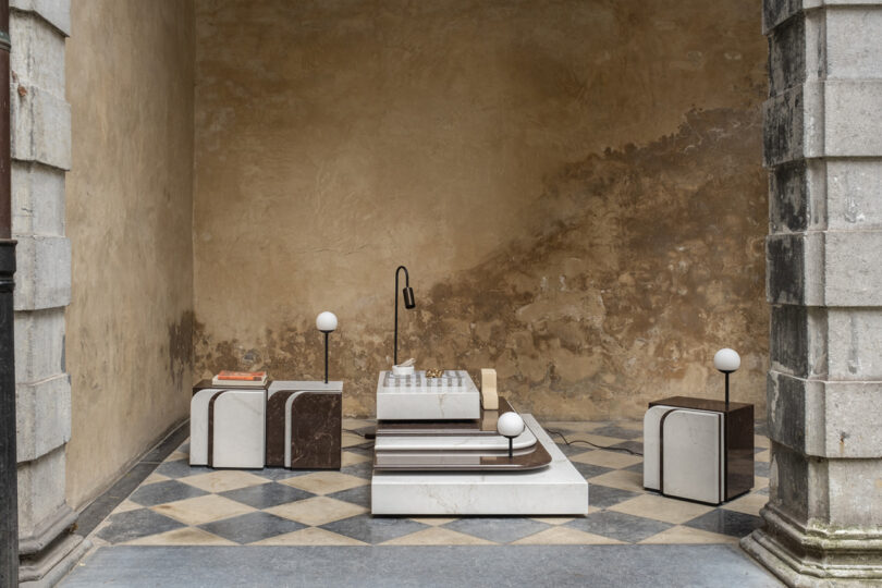 Modern geometric furniture set with marble texture arranged on a checkered floor against a rustic, textured wall.