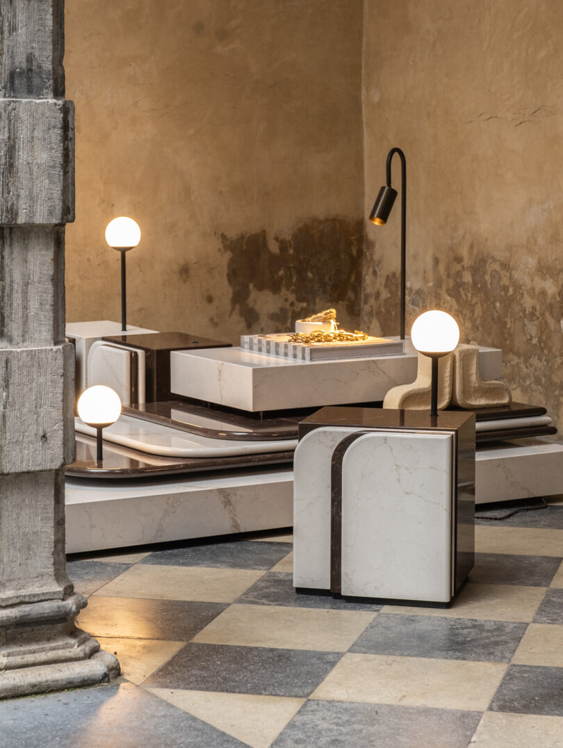 Modern furniture featuring geometric marble structures, round light fixtures, and a black floor lamp on a checkered tile floor against a textured wall.