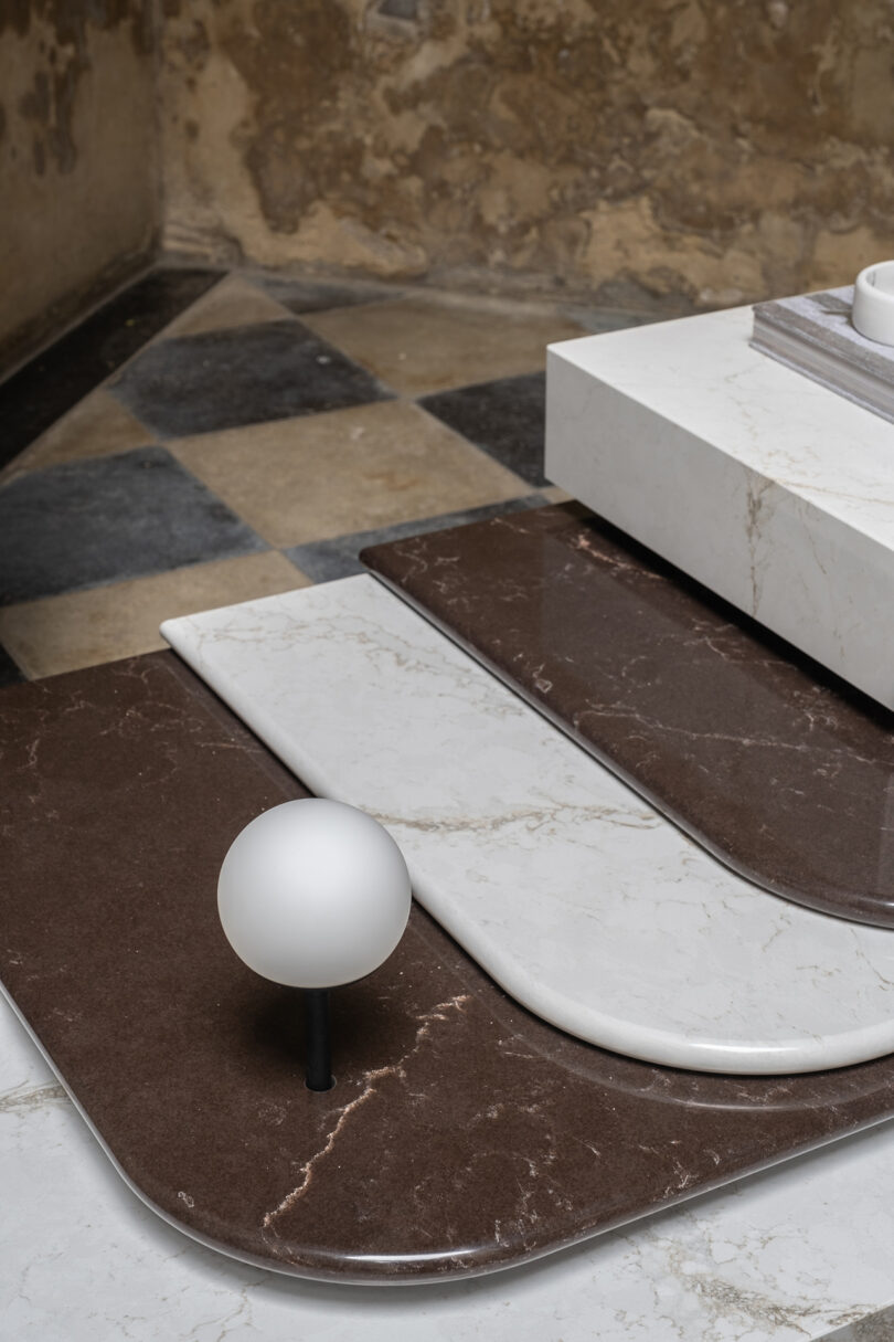 Geometric marble platforms with a spherical lamp on a checkered floor.