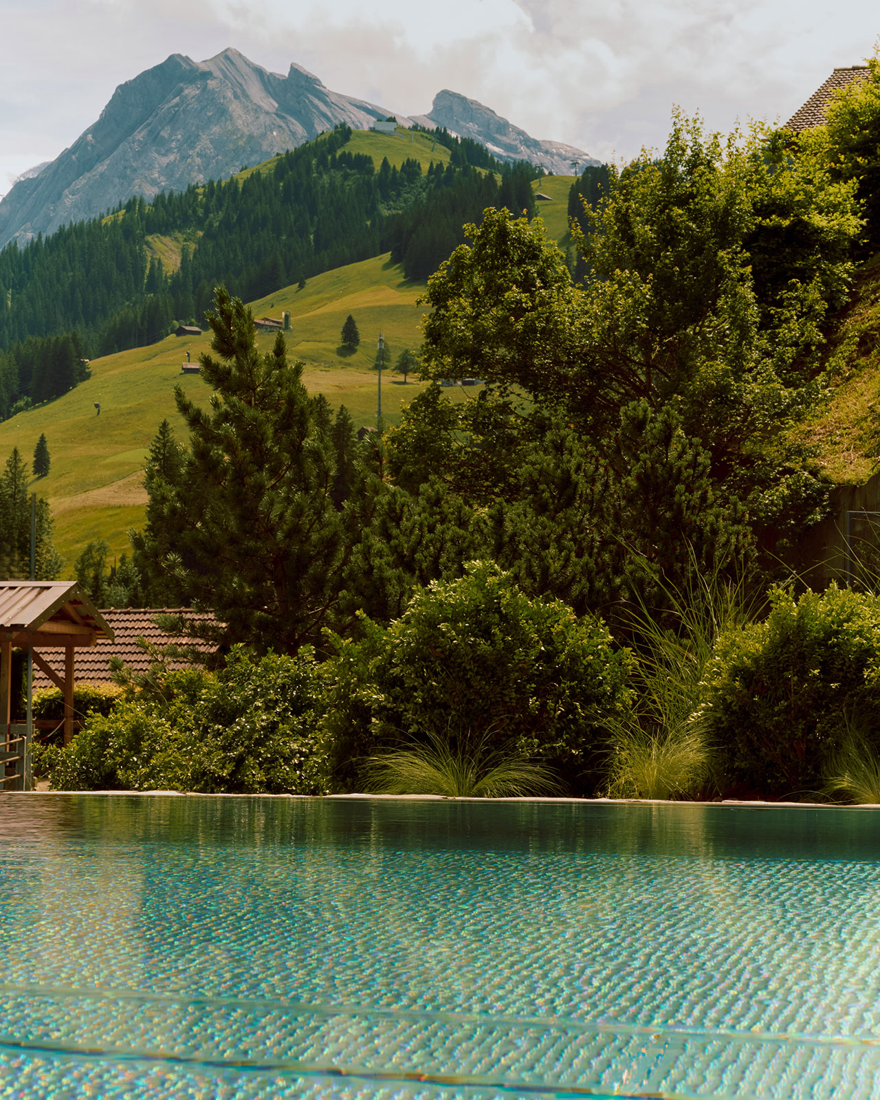 Mountains and greenery in the background with a calm blue swimming pool reflecting sunlight in the foreground.