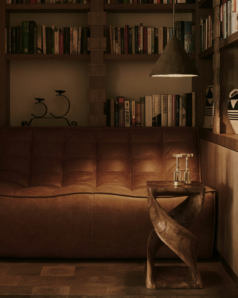 A cozy room with a brown leather sofa, bookshelves, a small wooden table with a vintage telephone, and a hanging lamp casting a warm light.