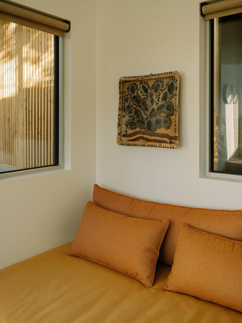 A cozy room with a tan daybed, two matching pillows, two windows, and a decorative wall hanging.