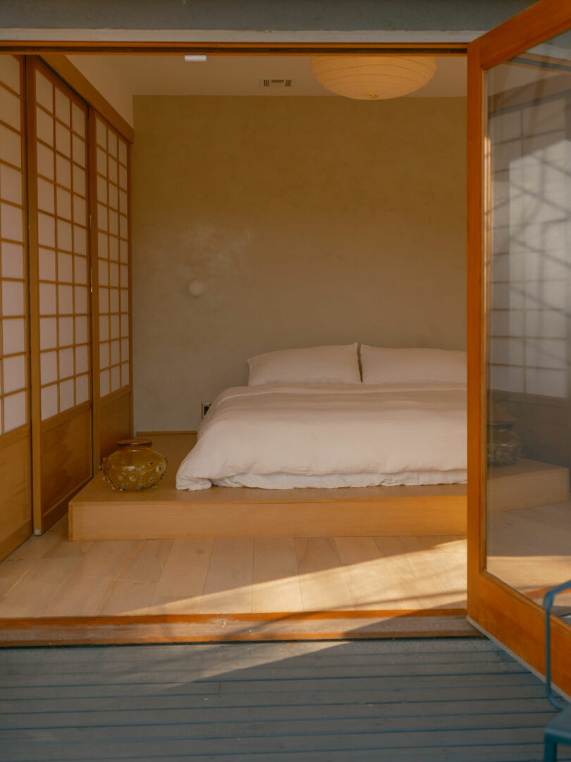 A minimalist bedroom with a futon-style bed, sliding shoji doors, and warm natural lighting.