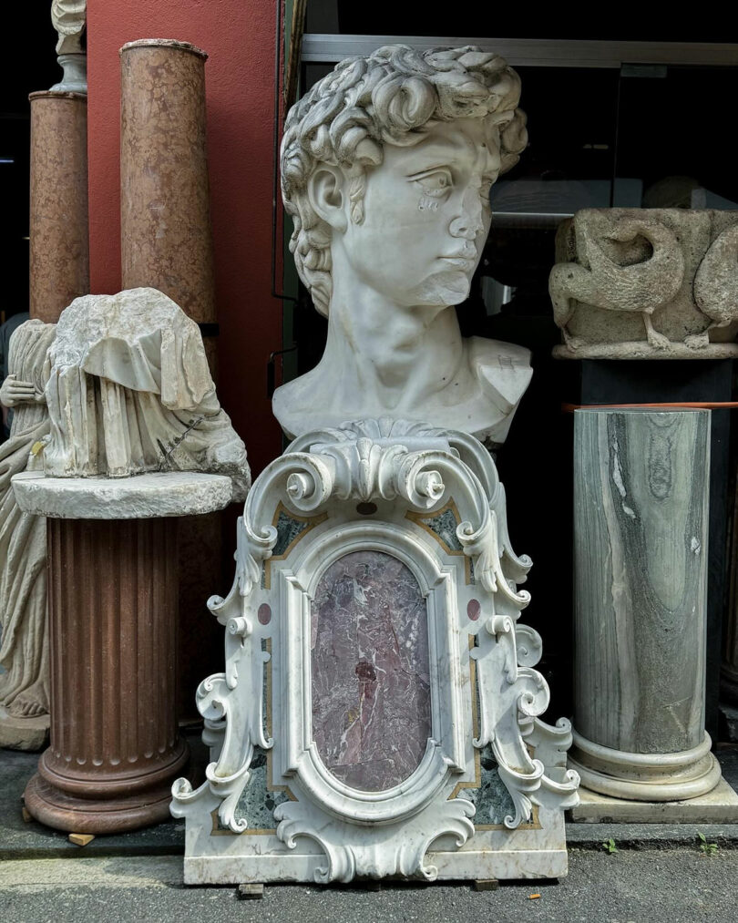 A collection of sculptural pieces, including a large bust, several columns, and an ornate frame, displayed outside.