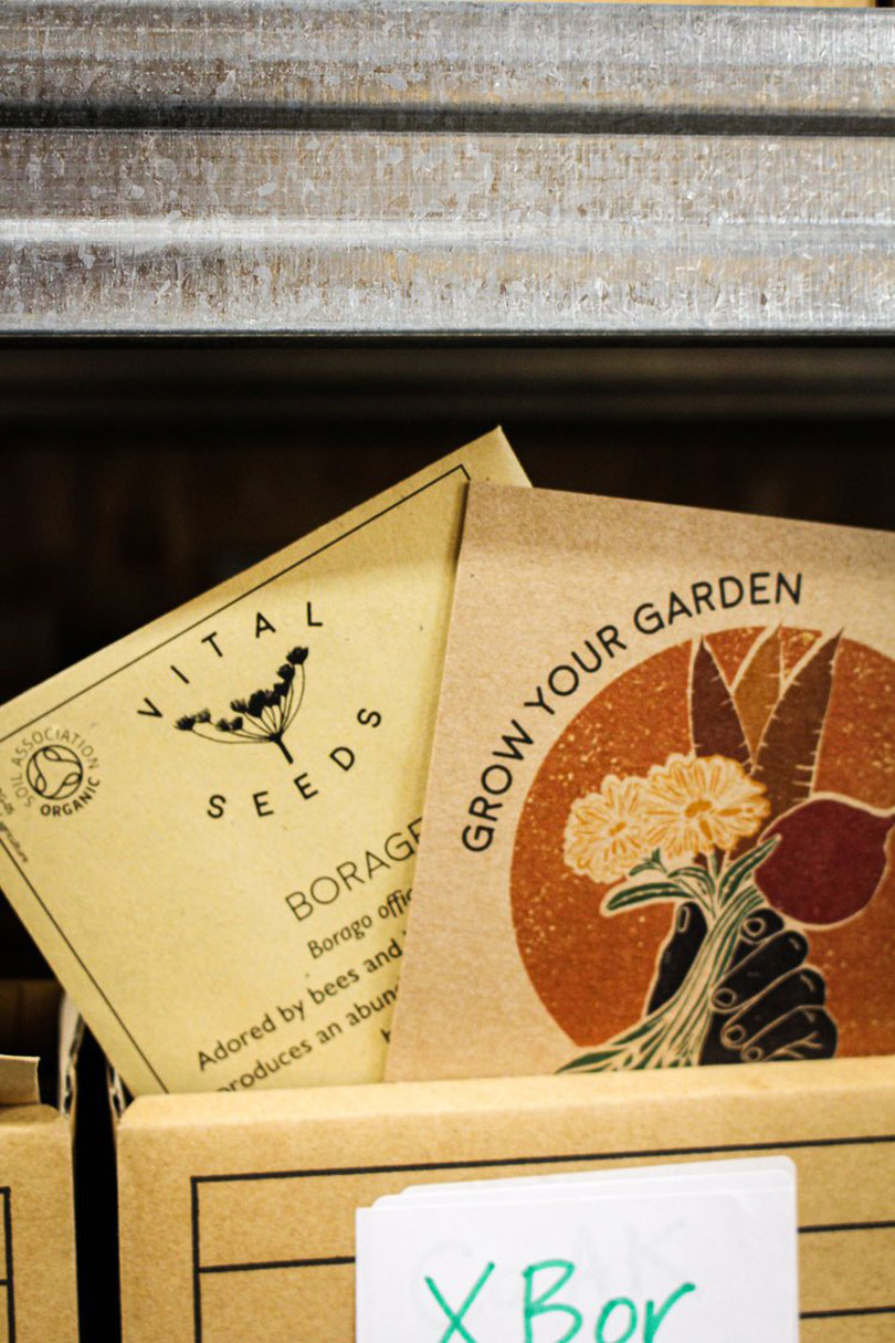 Packets of seeds, labeled "Vital Seeds" and "Grow Your Garden," designed by Richard Parr, are neatly displayed on a shelf.