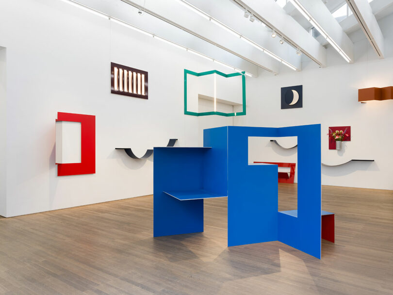 A modern art gallery with colorful geometric sculptures and wall art, featuring red, blue, and green shapes on wooden flooring