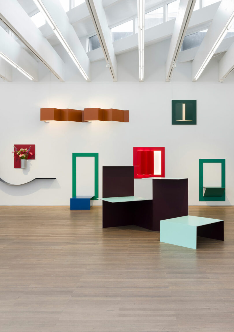 Geometric art installation in a gallery with colorful shapes and mirrored surfaces on a wooden floor