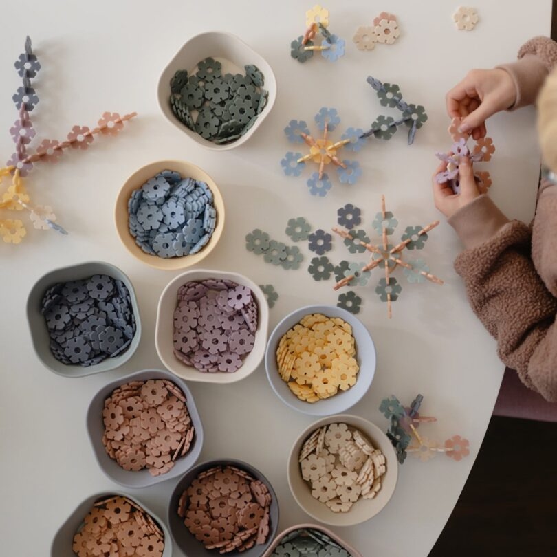 Person assembling interlocking flower-shaped pieces at a table, with several bowls of colorful pieces nearby