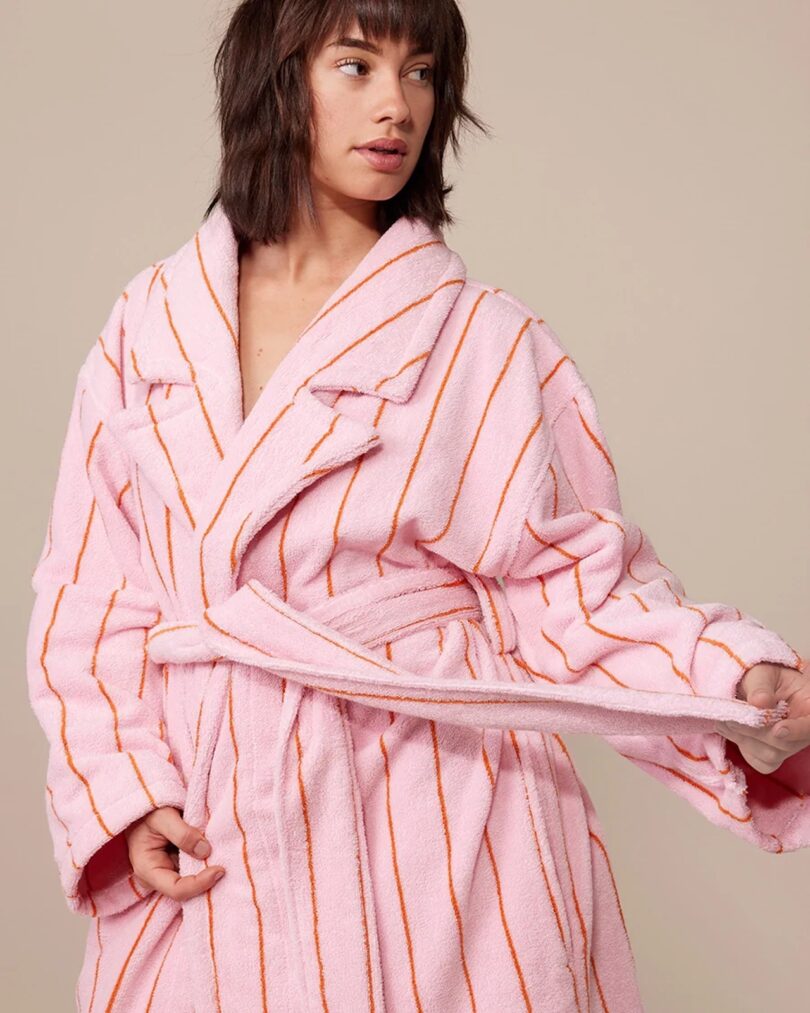 A woman with short hair wearing a Hommey robe in the Fleur print (pink with orange pinstripe