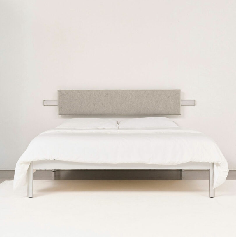 Minimalist bed with a gray headboard, white bedding, and metal frame on a light-colored floor.