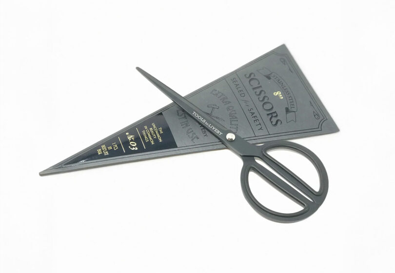 Black scissors with a unique triangular paper packaging featuring text and design elements on a white background.