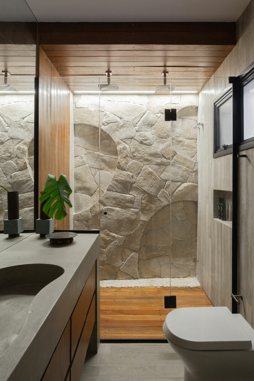 Modern bathroom with a stone wall shower, glass door, wooden floor, and countertop with a leaf decoration.