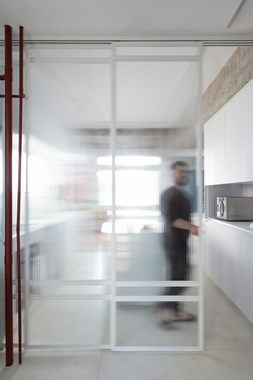 A person standing behind a frosted glass sliding door in a modern kitchen with white cabinets and a microwave.