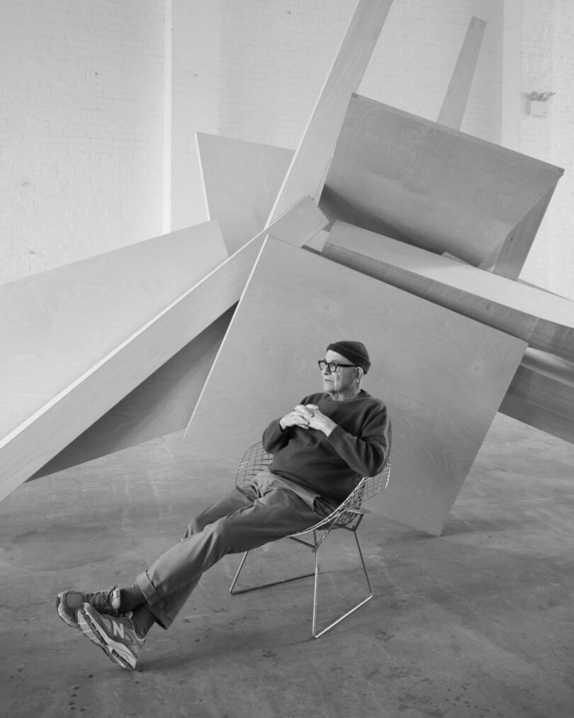 Man sits in front of large abstract wood sculpture