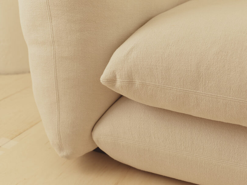 Close-up of a beige fabric sofa with plush cushions, resting on a light wooden floor.