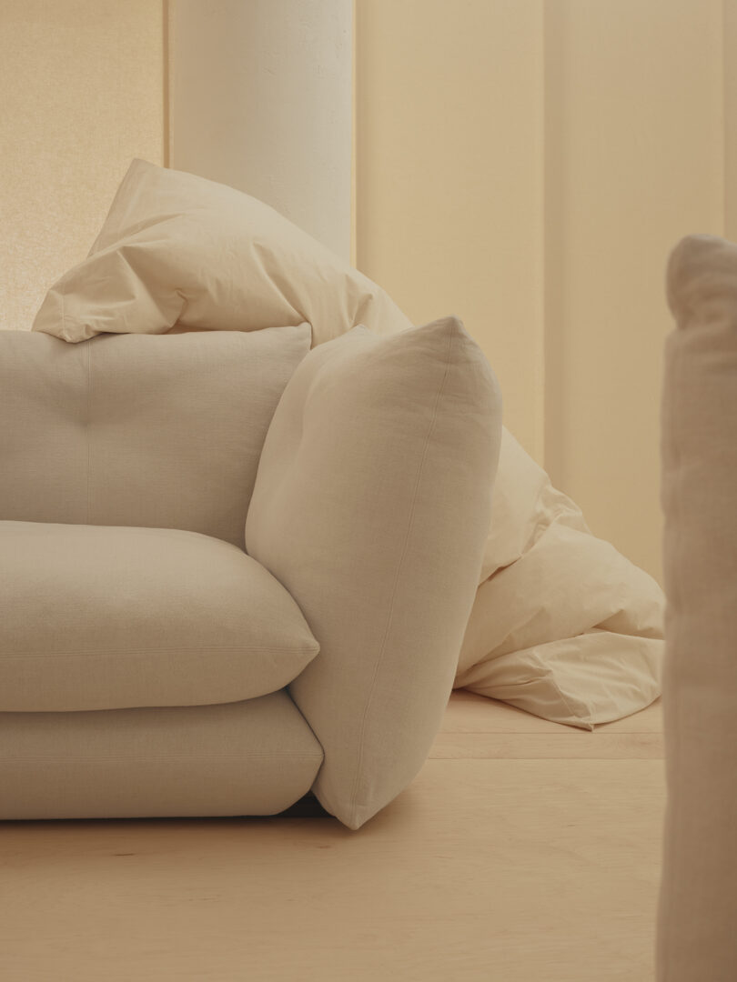 A beige sofa with plush cushions is positioned in a softly lit room, complemented by beige fabric panels in the background.