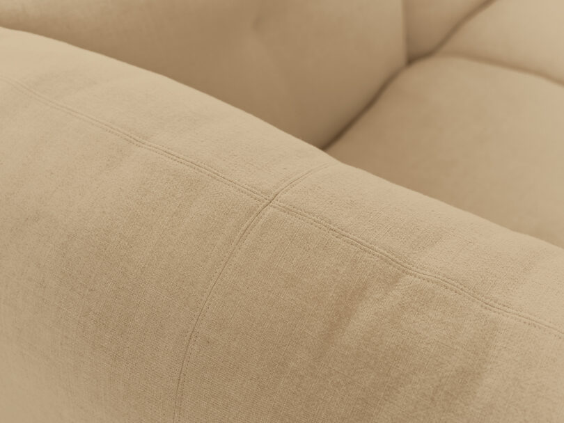 Close-up view of a beige upholstered sofa armrest with visible stitching details.