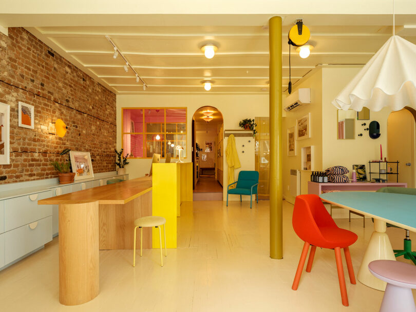 A colorful, modern room with a wooden table, vibrant chairs, exposed brick wall, and eclectic decor.