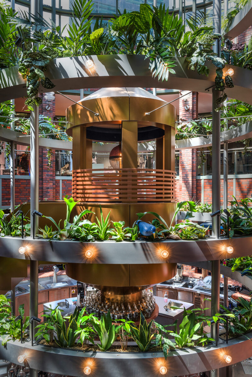 A multi-level atrium with lush green plants and modern design elements, featuring circular walkways and natural lighting.