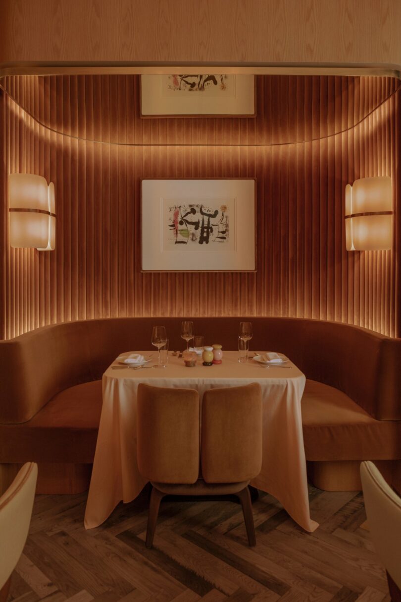 Elegant restaurant booth with a round table, set for two, featuring warm lighting, upholstered seats, and a framed artwork on the wall.