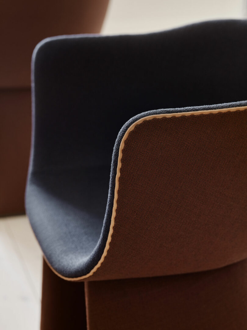 Close-up of a modern chair with brown and dark gray fabric, featuring a curved backrest and beige stitching along the edge.