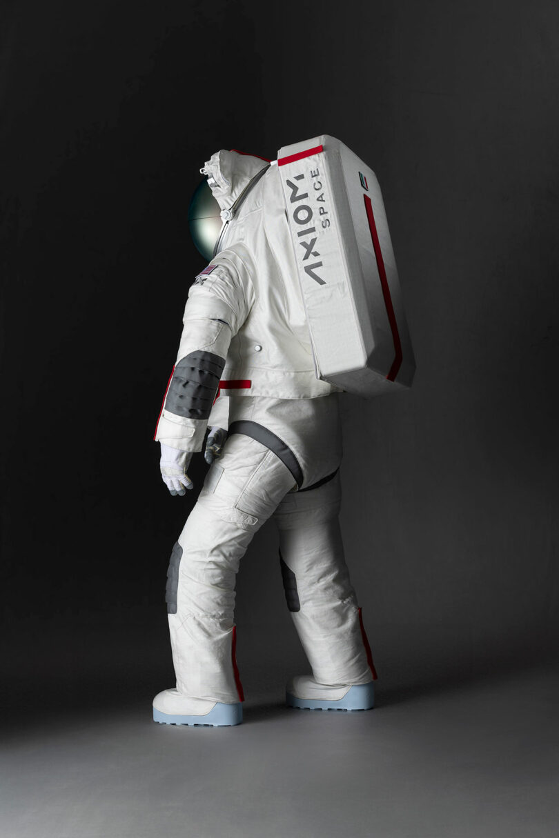 A person wearing a white spacesuit with "Axiom Space" printed on it stands against a dark background.