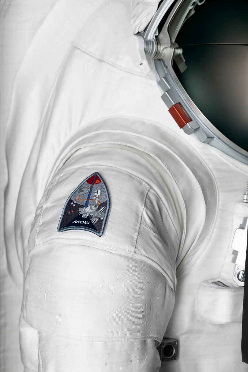 Close-up of an astronaut suit displaying a shoulder patch with space-related imagery and a helmet reflecting light.