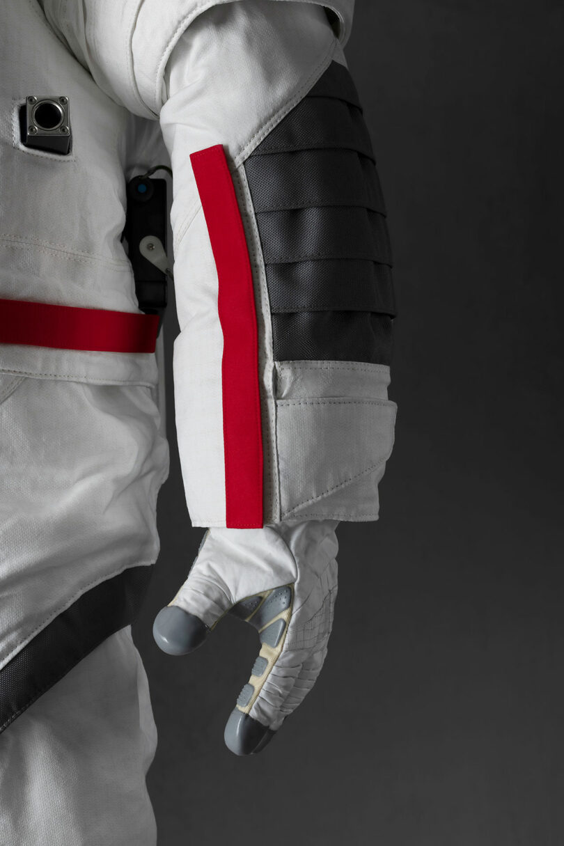 A close-up of an astronaut suit's arm, featuring a red stripe and ribbed black padding on a grey background.