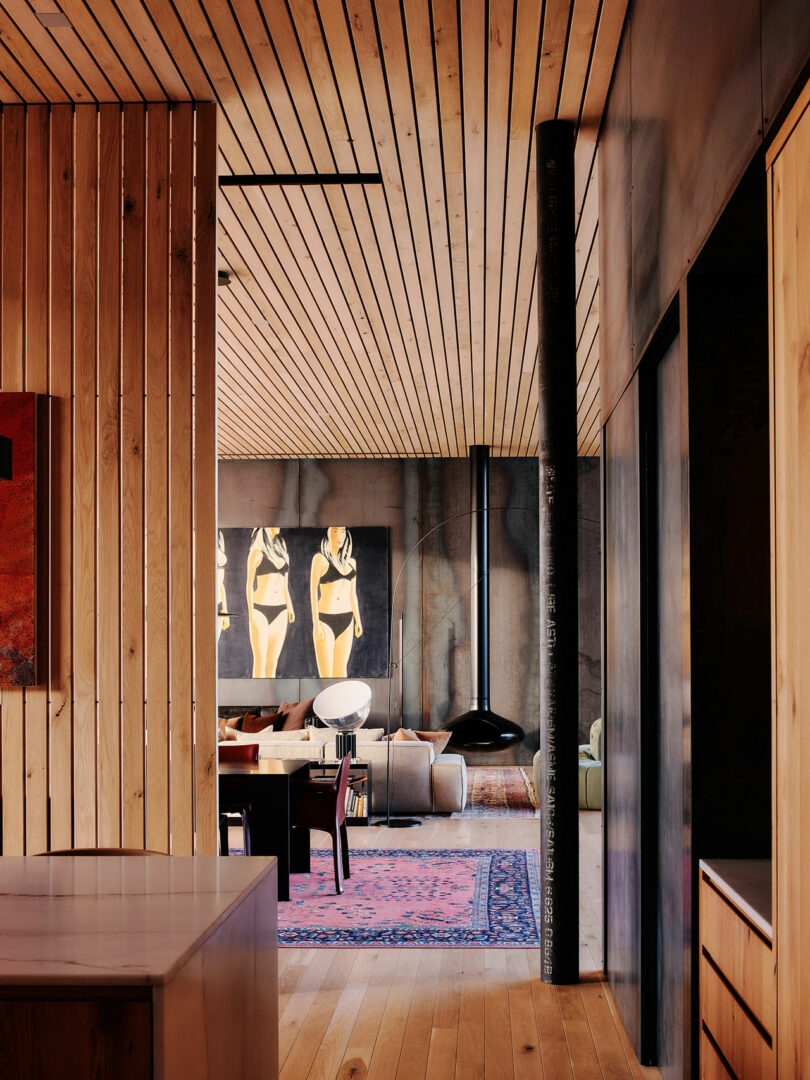 A modern living room with wooden walls and ceiling, contemporary artwork, dark furniture, and a patterned rug on the floor. The space has a minimalistic yet artistic design.