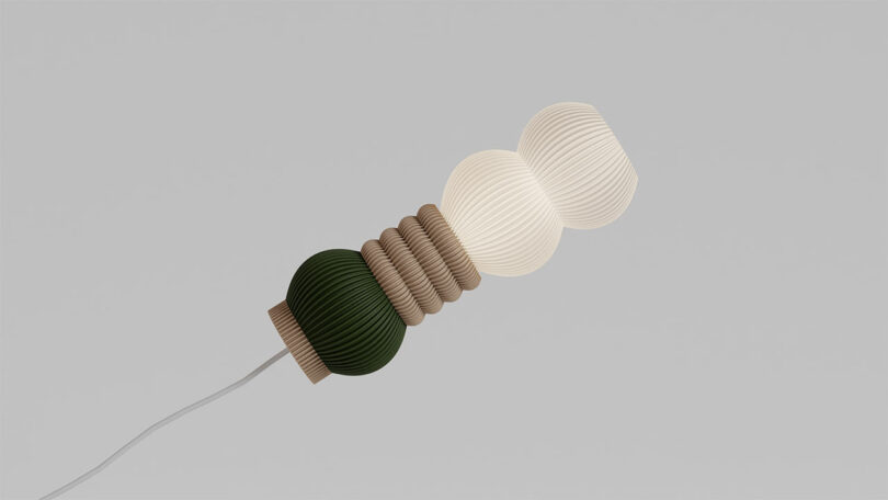 The STAK Modular Lamp is a decorative light fixture with a stacked design featuring three distinct sections: a dark green base, a beige middle, and a glowing white top. This elegant fixture seamlessly connects to a white cord.