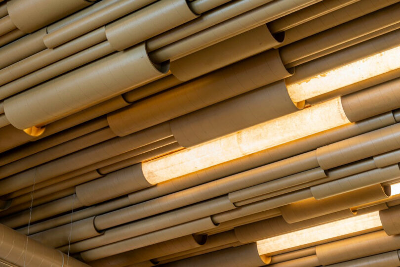 A ceiling design featuring numerous cylindrical tubes arranged parallel to each other, with some cylinders illuminated from within, creating a pattern of light and shadows.