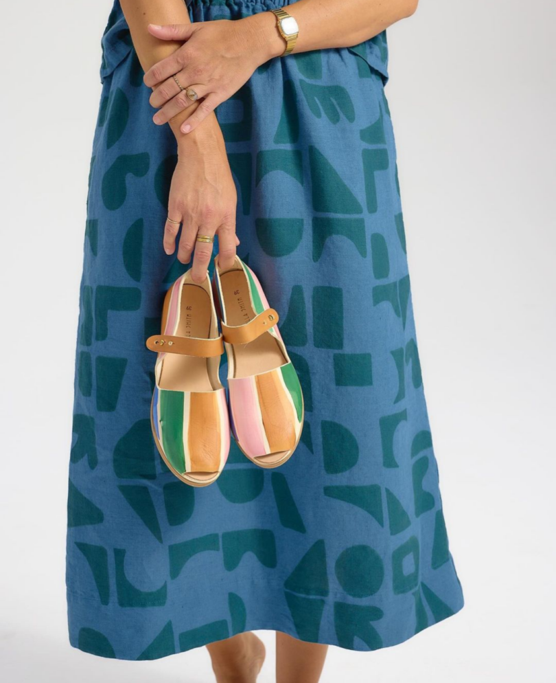 A person in a blue patterned dress holds a pair of colorful sandals, reminiscent of a vibrant Take 5 summer getaway.