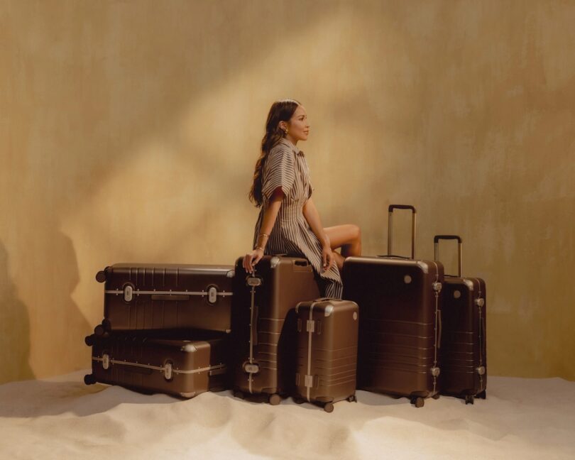 Multiple brown luggages from Monos displayed with collaborator Julie Sariñana of Sincerely Jules sitting on top