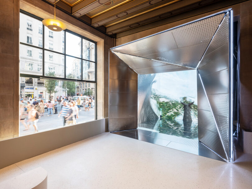 Modern interior with a large geometric metallic installation and a wide window showing a busy street outside.