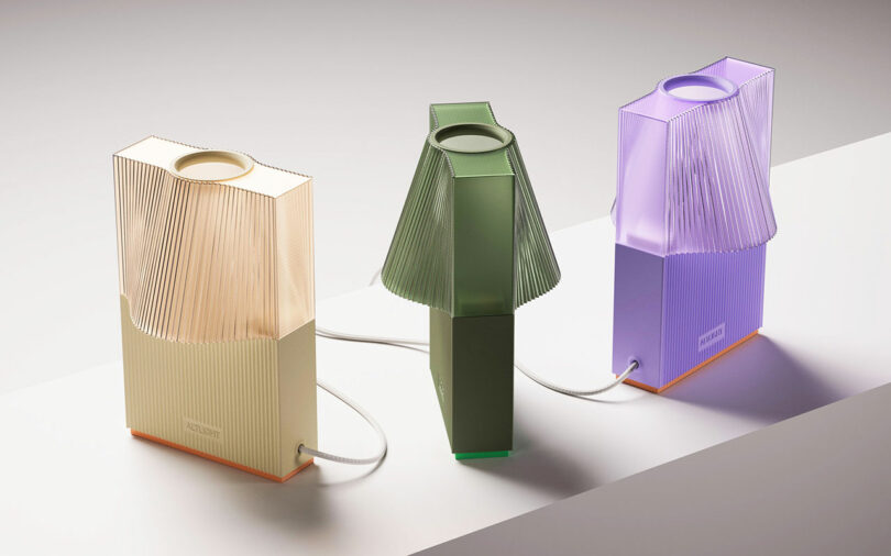 Three modern ALT Light lamps with pleated paper shades in beige, green, and purple are elegantly arranged on a white surface, all connected by a sleek cord.