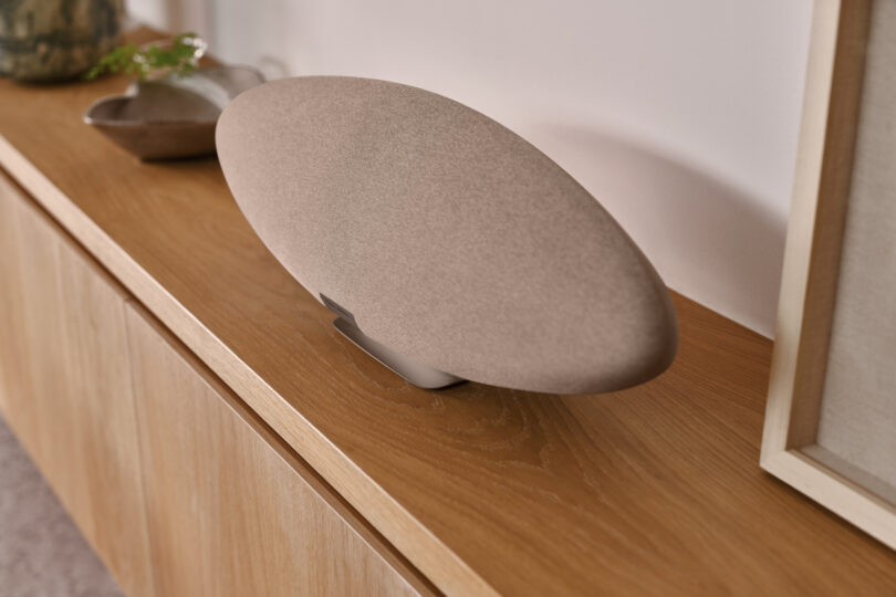 A sleek, oval-shaped speaker on a wooden cabinet with a minimalist design.