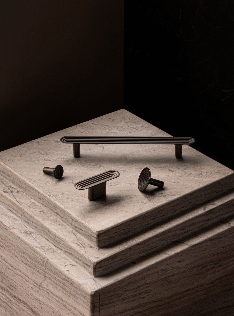 A set of minimalist black handles displayed on stacked marble slabs in a dark setting