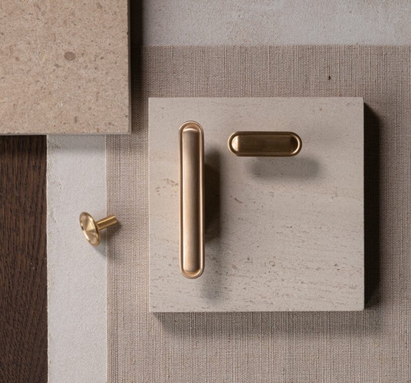 Top-view of modern brass cabinet handles and a knob on a beige textured background with a wooden accent