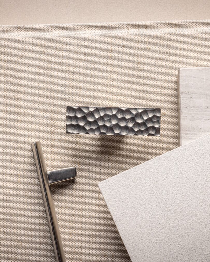 Textured metal cabinet handle on a beige background with samples of stone and textured white material nearby