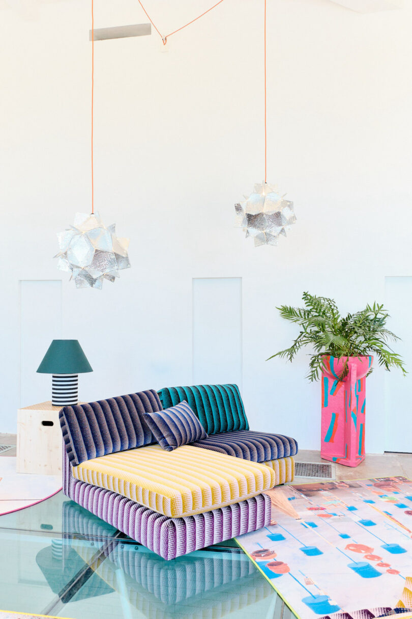 Colorful modern living room with a striped sofa, geometric rug, two star-shaped pendant lights, and a large planter with greenery